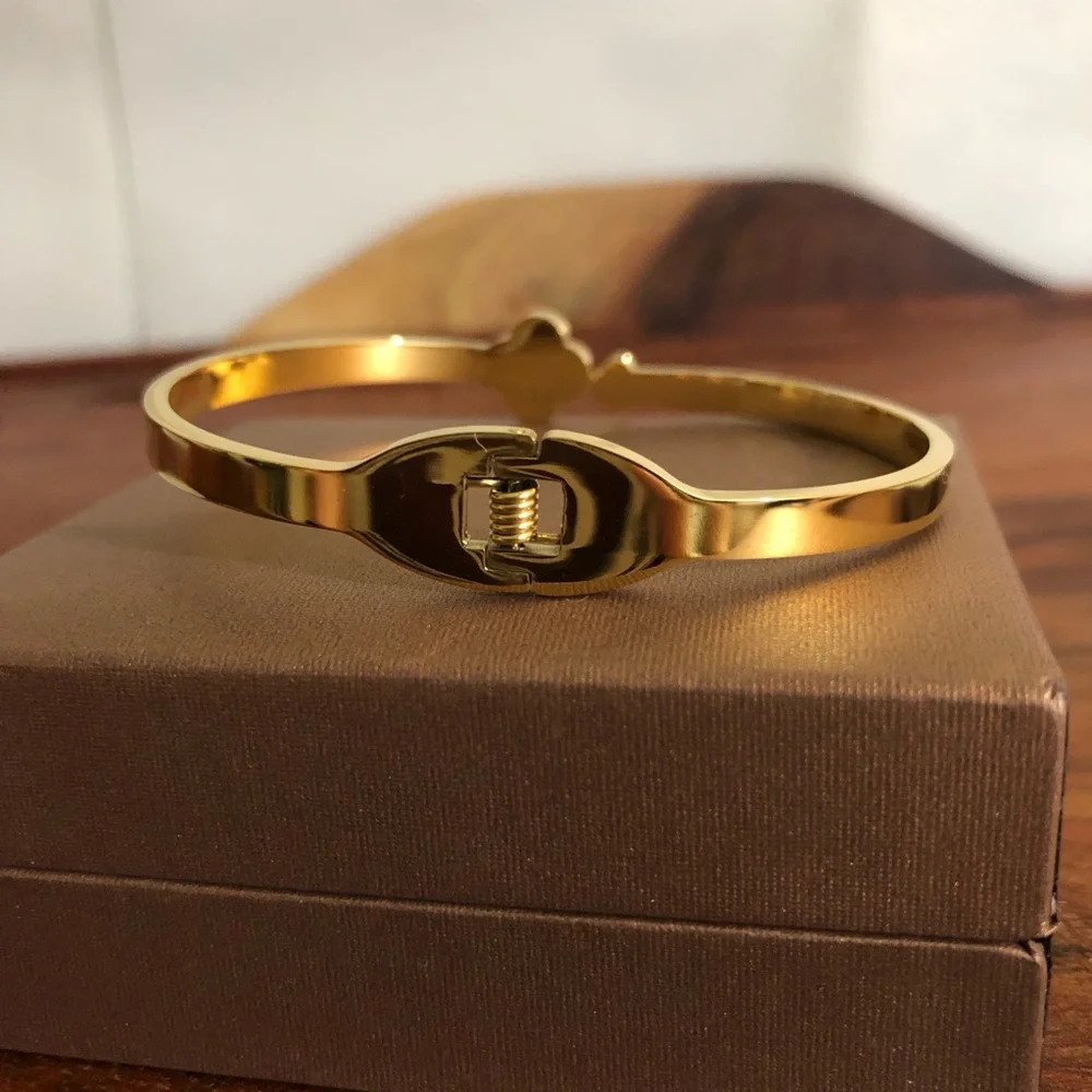gold-toned hinged bangle bracelet featuring white clover motifs and crystal New